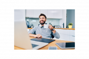 Young man holding a cup of coffee smiling while seated at his home office desk