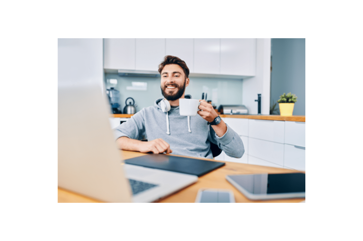 Young man holding a cup of coffee smiling while seated at his home office desk